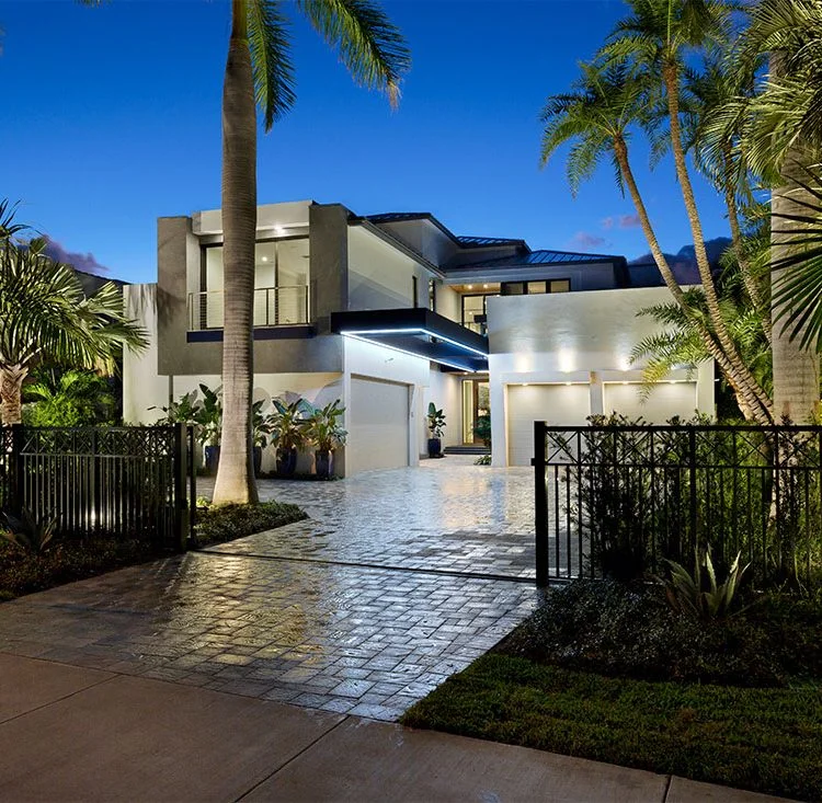Modern home at dusk with a stone driveway and palms