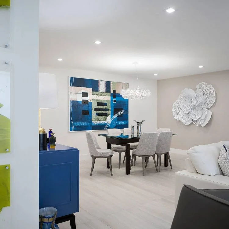 Dining area with blue artwork, upholstered chairs, and sculptural wall decor