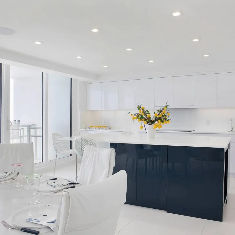 White kitchen with a dark blue island beside a glass dining table