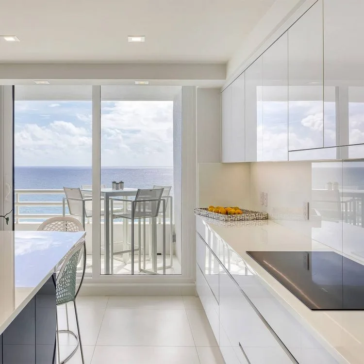 Glossy white kitchen looking through glass doors to the ocean