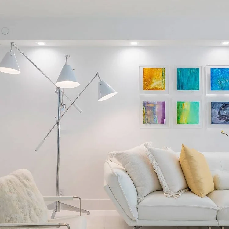 Colorful small paintings above a white sofa with yellow cushions